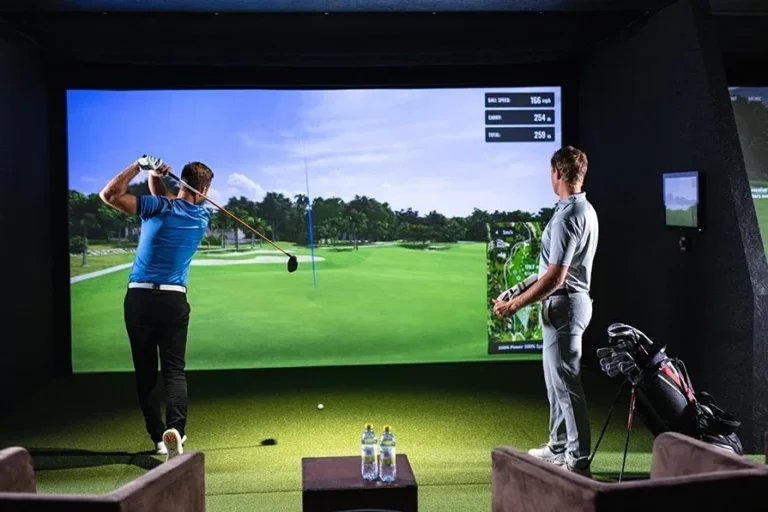 Indoor golf lesson using a simulator as a coach observes ball flight on screen