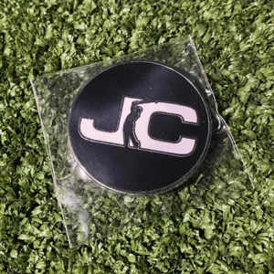 JC Golf Studio golf ball marker with John Collins Golf branding on back displayed on turf in Queensland