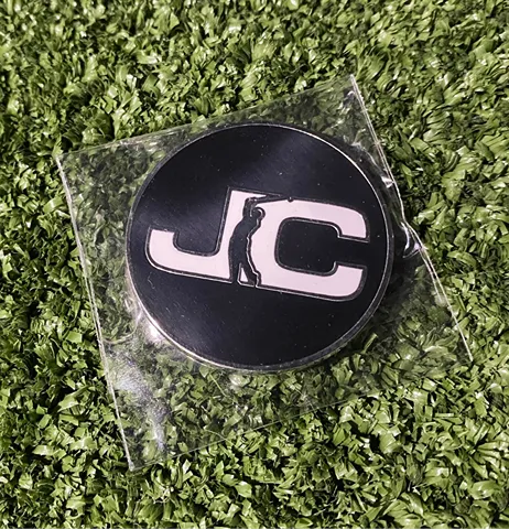 JC Golf Studio golf ball marker with John Collins Golf branding on back displayed on turf in Queensland