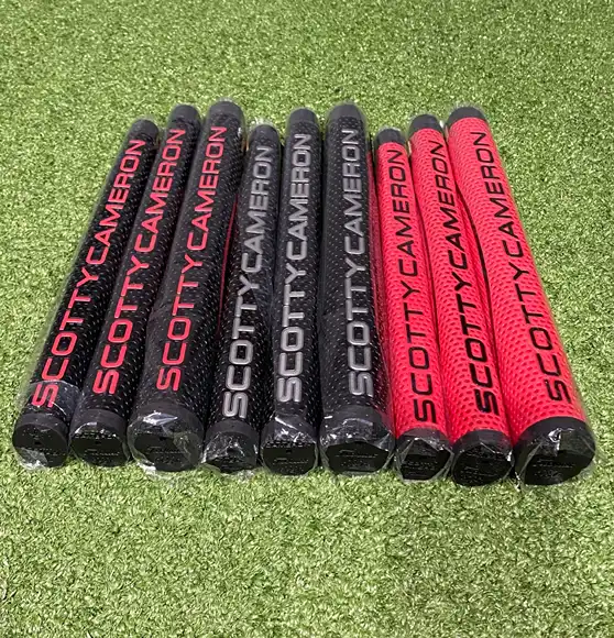 Angled display of red and black Scotty Cameron putter grips on turf.