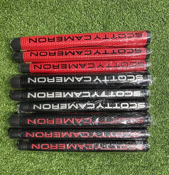 Assorted Scotty Cameron putter grips in red and black displayed on artificial turf.